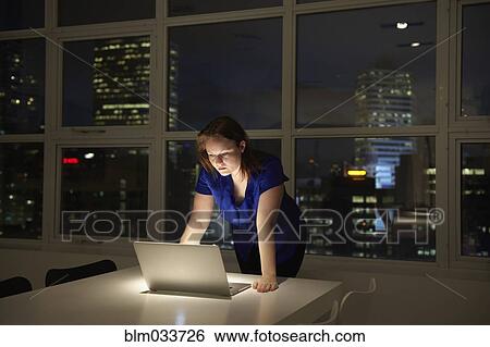 Stock Photograph - Caucasian businesswoman working on laptop in office at night. Fotosearch