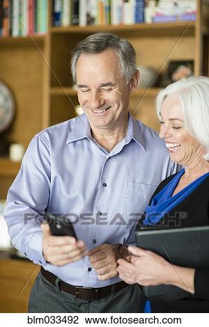Stock Image - Caucasian couple using cell phone in living room. Fotosearch