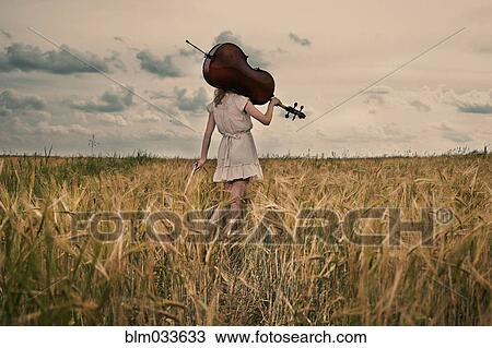 Stock Image - Caucasian girl carrying cello on shoulder in rural fieldCaption. Fotosearch