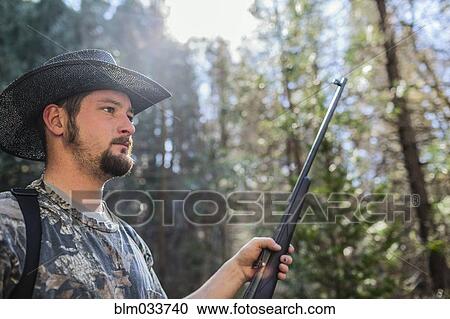 Stock Image - Caucasian hunter holding gun in forest. Fotosearch