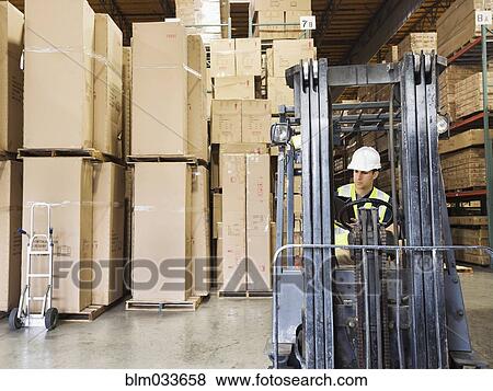 Stock Photo - Caucasian worker driving forklift in warehouse. Fotosearch