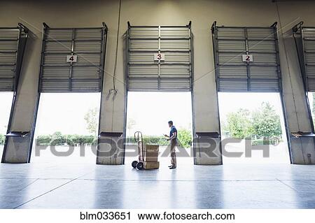 Stock Image - Caucasian worker examining cardboard boxes in warehouse. Fotosearch