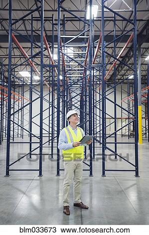 Stock Image - Caucasian worker using digital tablet in empty warehouse. Fotosearch