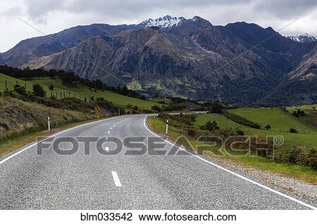 Stock Image - Empty road to mountains in remote landscape, Wanaka, Central Otago, New Zealand. Fotosearch