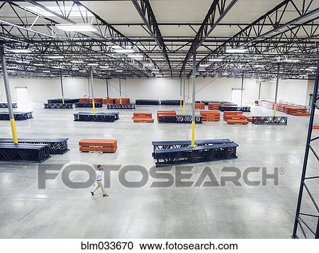 Stock Image - High angle view of Caucasian businessman walking in empty warehouse. Fotosearch