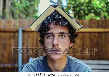 Stock Image - Hispanic man balancing book on head in backyard. Fotosearch