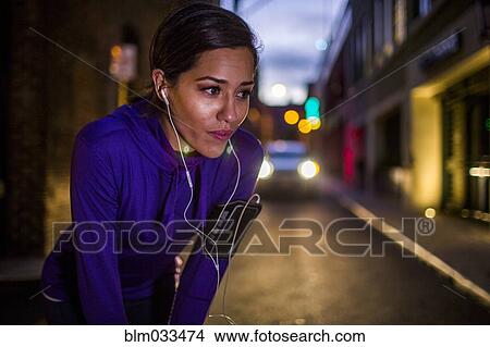 Hispanic runner resting on city street at night View Large Photo Image Picture - Hispanic runner resting on city street at night. Fotosearch