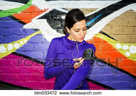 Stock Image - Hispanic runner using cell phone near graffiti wall. Fotosearch