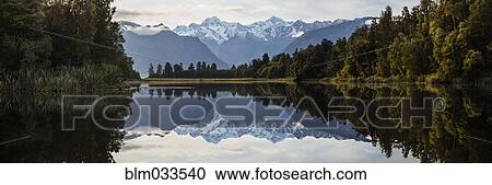 Stock Image - Mountains and forest reflecting in still lake, Mt Cook Village, South Westland, New Zealand. Fotosearch