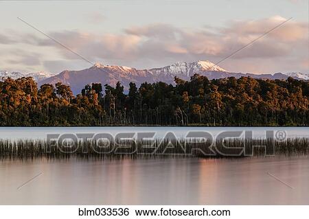 Stock Photograph - Mountains over forest and still river, Hokitika, South Westland, New Zealand. Fotosearch