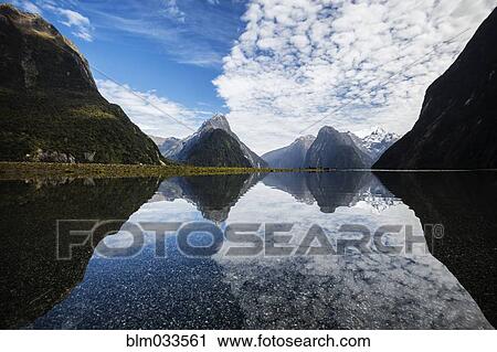 Stock Image - Mountains reflecting in remote lake, Milford Sound, Fiordland, New Zealand. Fotosearch