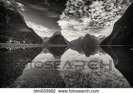 Stock Image - Mountains reflecting in remote lake, Milford Sound, Fiordland, New Zealand. Fotosearch