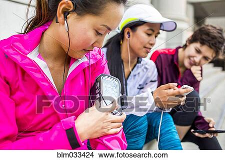 Runners using cell phones and earbud on city sidewalk View Large Photo Image Picture - Runners using cell phones and earbud on city sidewalk. Fotosearch