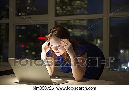 Stock Photography - Stressed Caucasian businesswoman working on laptop in office at night. Fotosearch