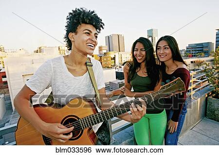 Woman playing guitar for friends on urban rooftop View Large Photo Image Stock Photograph - Woman playing guitar for friends on urban rooftop. Fotosearch