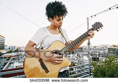 Stock Photo - Woman playing guitar on urban rooftop. Fotosearch