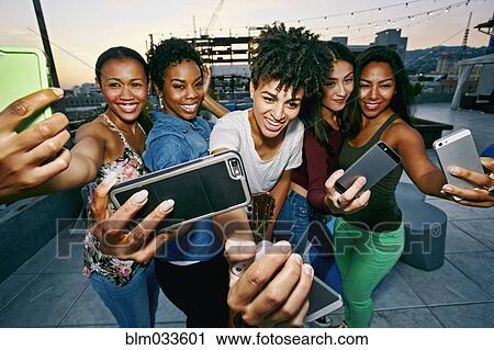 Stock Image - Women taking selfies with cell phones on urban rooftop. Fotosearch