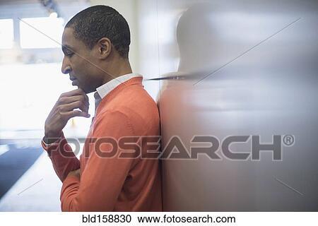 Stock Image - Black businessman leaning on wall. Fotosearch