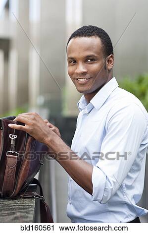 Stock Image - Black businessman opening briefcase outdoors. Fotosearch