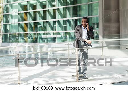 Stock Photo - Black businessman talking on cell phone outside building. Fotosearch