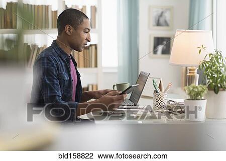 Stock Image - Black businessman using cell phone at desk. Fotosearch