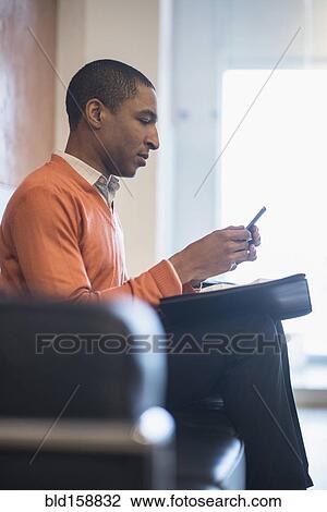 Stock Image - Black businessman using cell phone in office lobby. Fotosearch