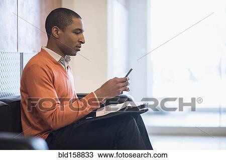 Stock Image - Black businessman using cell phone in office lobby. Fotosearch