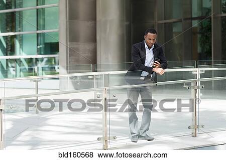 Stock Photo - Black businessman using cell phone outside building. Fotosearch