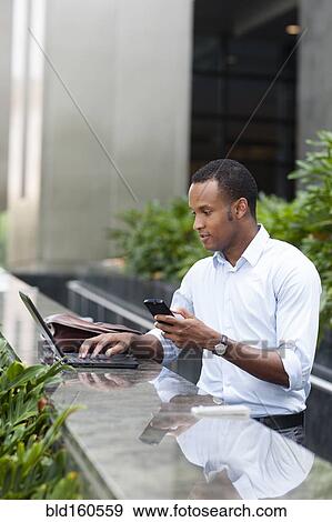 Black businessman using laptop and cell phone outdoors View Large Photo Image Stock Photo - Black businessman using laptop and cell phone outdoors. Fotosearch