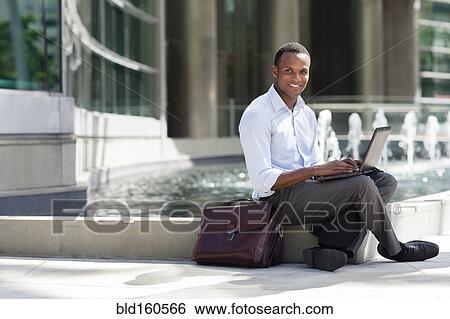 Black businessman using laptop near urban fountain View Large Photo Image Stock Photograph - Black businessman using laptop near urban fountain. Fotosearch