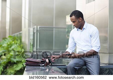 Stock Image - Black businessman using laptop outside building. Fotosearch