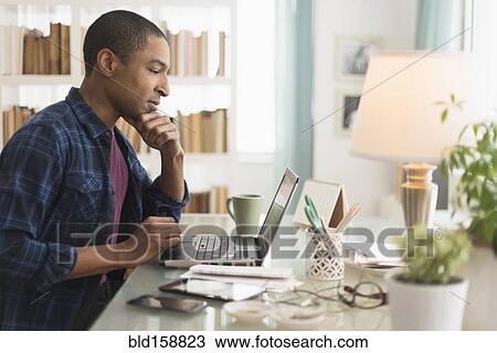 Stock Image - Black businessman working on laptop at desk. Fotosearch