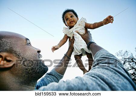 Black father holding baby daughter under blue sky View Large Photo Image Stock Image - Black father holding baby daughter under blue sky. Fotosearch