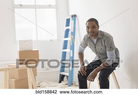 Stock Image - Black man sitting in room under renovation. Fotosearch