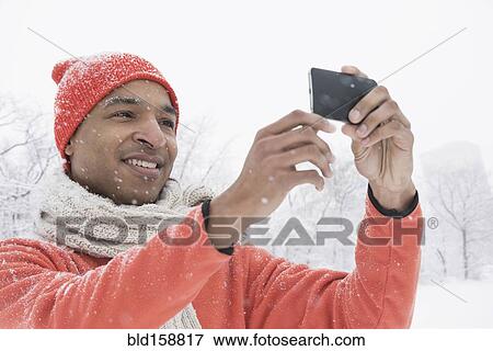 Stock Photo - Black man using cell phone in snow. Fotosearch