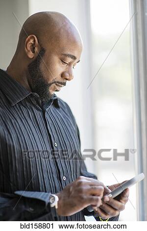 Stock Image - Black man using cell phone near window. Fotosearch