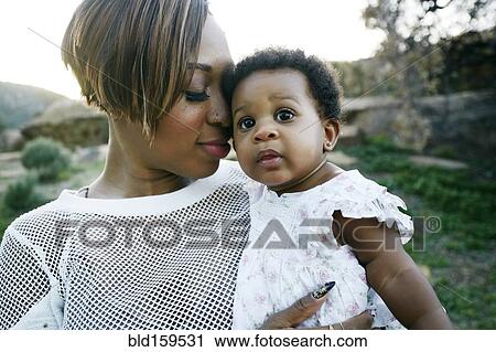 Stock Image - Black mother holding baby daughter in field. Fotosearch