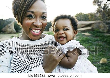 Stock Image - Black mother holding baby daughter in field. Fotosearch