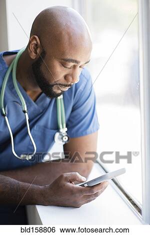 Black nurse using cell phone near window View Large Photo Image Stock Photograph - Black nurse using cell phone near window. Fotosearch
