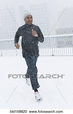 Stock Image - Black runner jogging in snow. Fotosearch