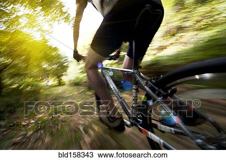 Stock Image - Blurred view of Caucasian man riding dirt bike in forest. Fotosearch