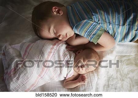 Stock Image - Boy napping with newborn sibling on bed. Fotosearch