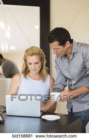 Stock Image - Business people drinking coffee and using laptop at desk. Fotosearch