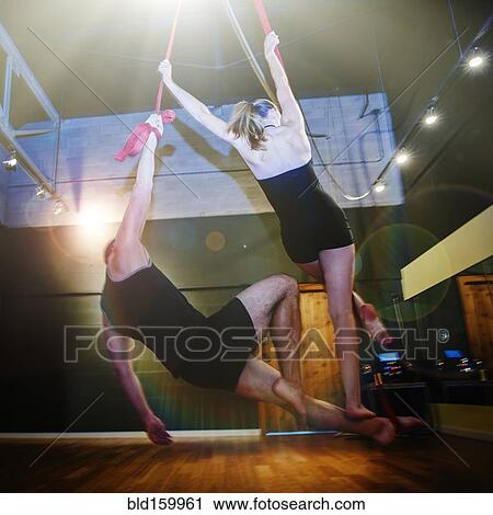 Stock Image - Caucasian acrobats hanging from ropes in studio. Fotosearch