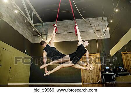 Stock Photograph - Caucasian acrobats hanging from ropes in studio. Fotosearch