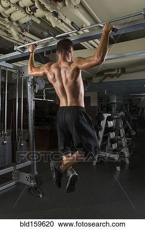 Stock Image - Caucasian athlete doing pull-ups in gymnasium. Fotosearch