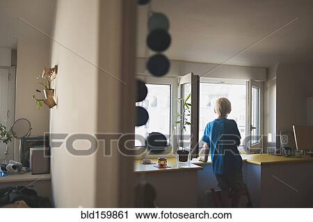 Stock Image - Caucasian boy looking out kitchen window. Fotosearch