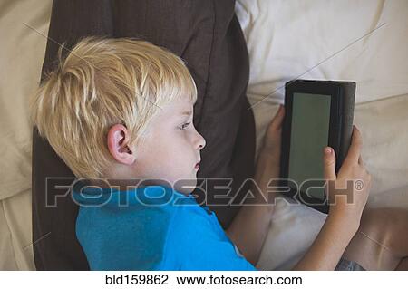 Stock Image - Caucasian boy reading digital tablet in bed. Fotosearch