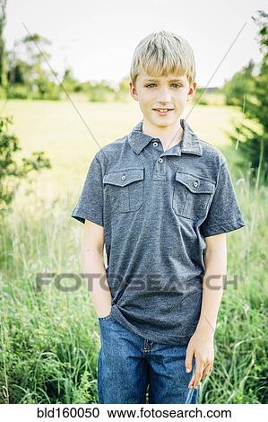 Stock Image - Caucasian boy standing in tall grass field. Fotosearch