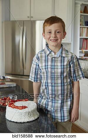 Stock Photo - Caucasian boy standing with cake in kitchen. Fotosearch